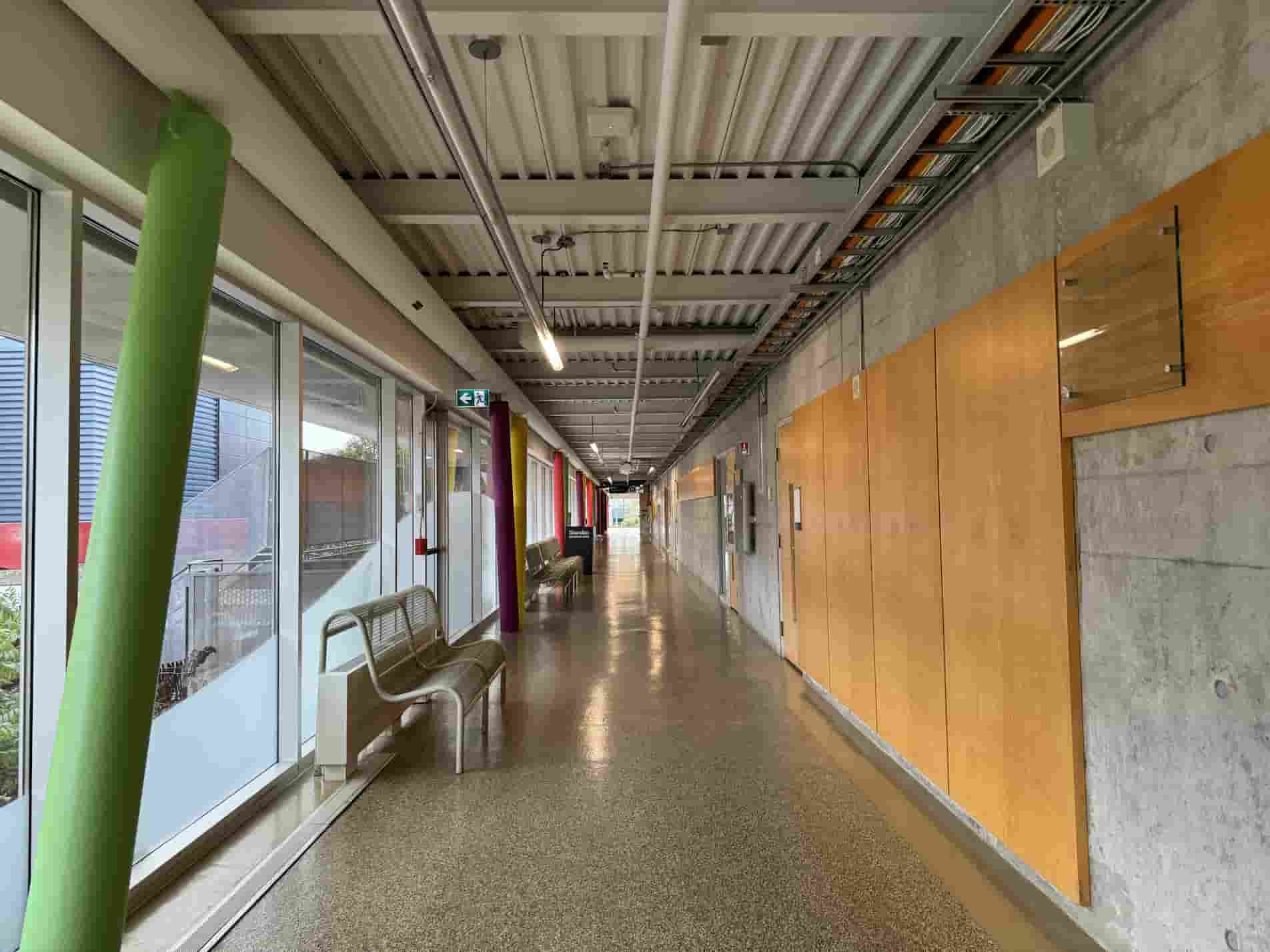 Image of the interior of the H-wing – This hallway contrasts colourful diagonal columns on the left with a clean and structured design on the right. The use colours adds emotional warmth , while the geometric architecture expresses clarity. Together, these two design languages balance emotion and structure.